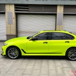 Side profile close-up BMW 3 Series with MOZX Gloss Neon Lime glossy TPU wrap, door and wheel arch seamless install detail