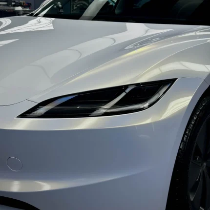 MOZX Easy White Iridescent Gold PET vinyl wrap close-up on Tesla Model 3 front headlight hood, golden color shift high gloss surface