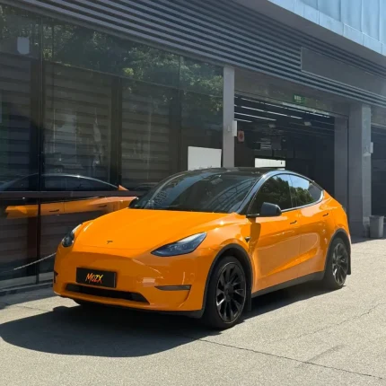 Macro close-up Tesla T trunk badge on MOZX Easy McLaren Orange PET vinyl wrap, zero orange peel ultra-smooth high gloss surface