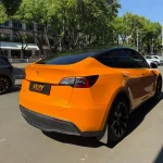 Rear wheel arch close-up Tesla Model Y wrapped MOZX Easy McLaren Orange PET wrap, perfect film conformity on curved fender