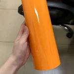 Handheld raw roll sample of MOZX Smart McLaren Orange high gloss PET vinyl wrap, saturated racing orange smooth mirror surface