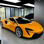 Three-quarter front shot McLaren sports car wrapped with MOZX Elite McLaren Orange glossy TPU wrap, factory-level paint finish color change film