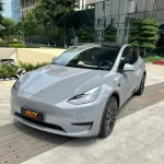 Tesla Model Y wrapped in MOZX Easy Nardo Grey high-gloss PET vinyl wrap, modern business plaza full front exterior shot