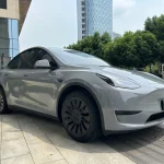 Side fender wheel arch close-up of Tesla Model Y wrapped MOZX Easy Nardo Grey glossy PET wrap, smooth uniform grey coverage on curved EV body panels